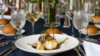 Meal place setting with fish, wine, water, and a bread roll.